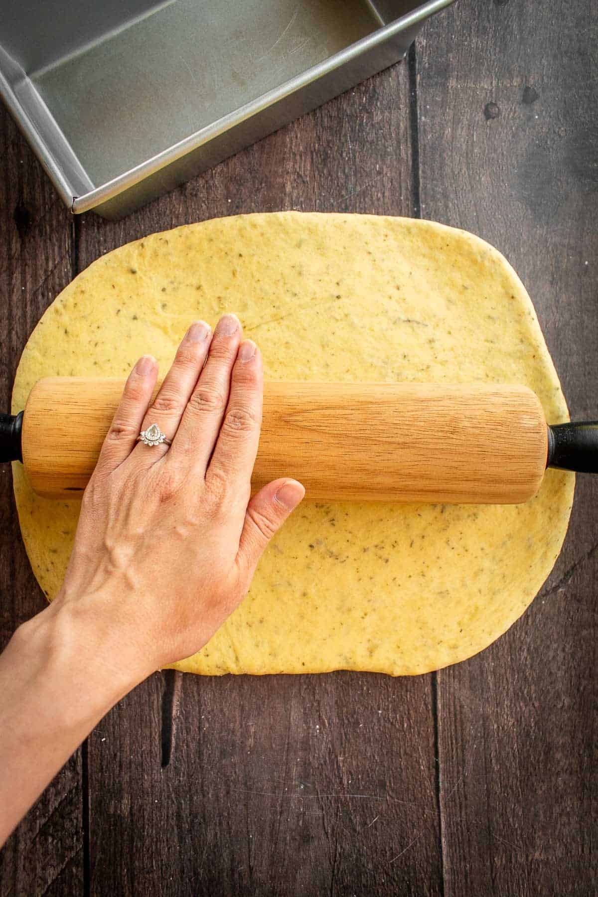 A hand rolling out bread dough with a rolling pin.