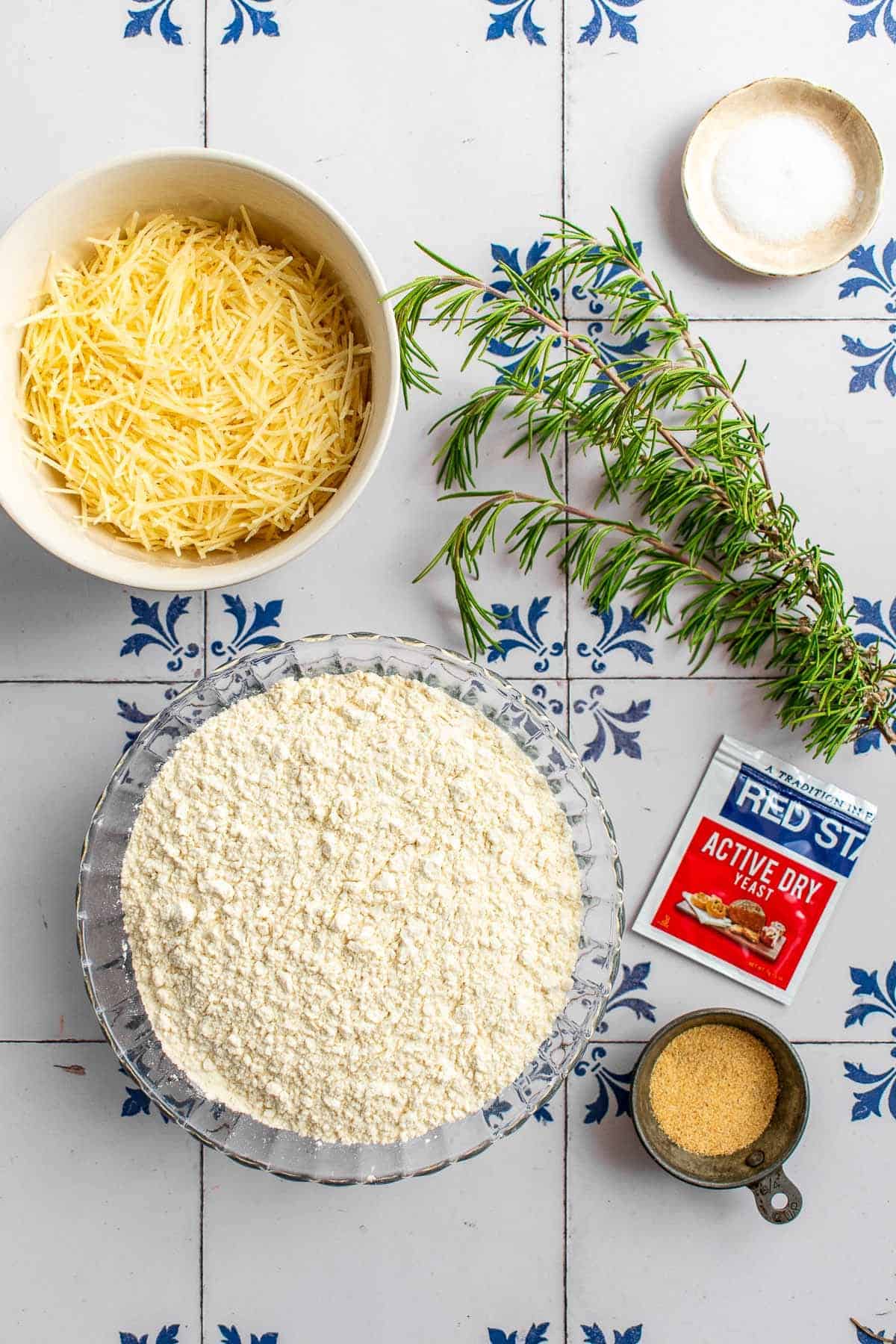 Bowls of flour, parmesan, salt, and garlic powder next to sprigs of fresh rosemary.