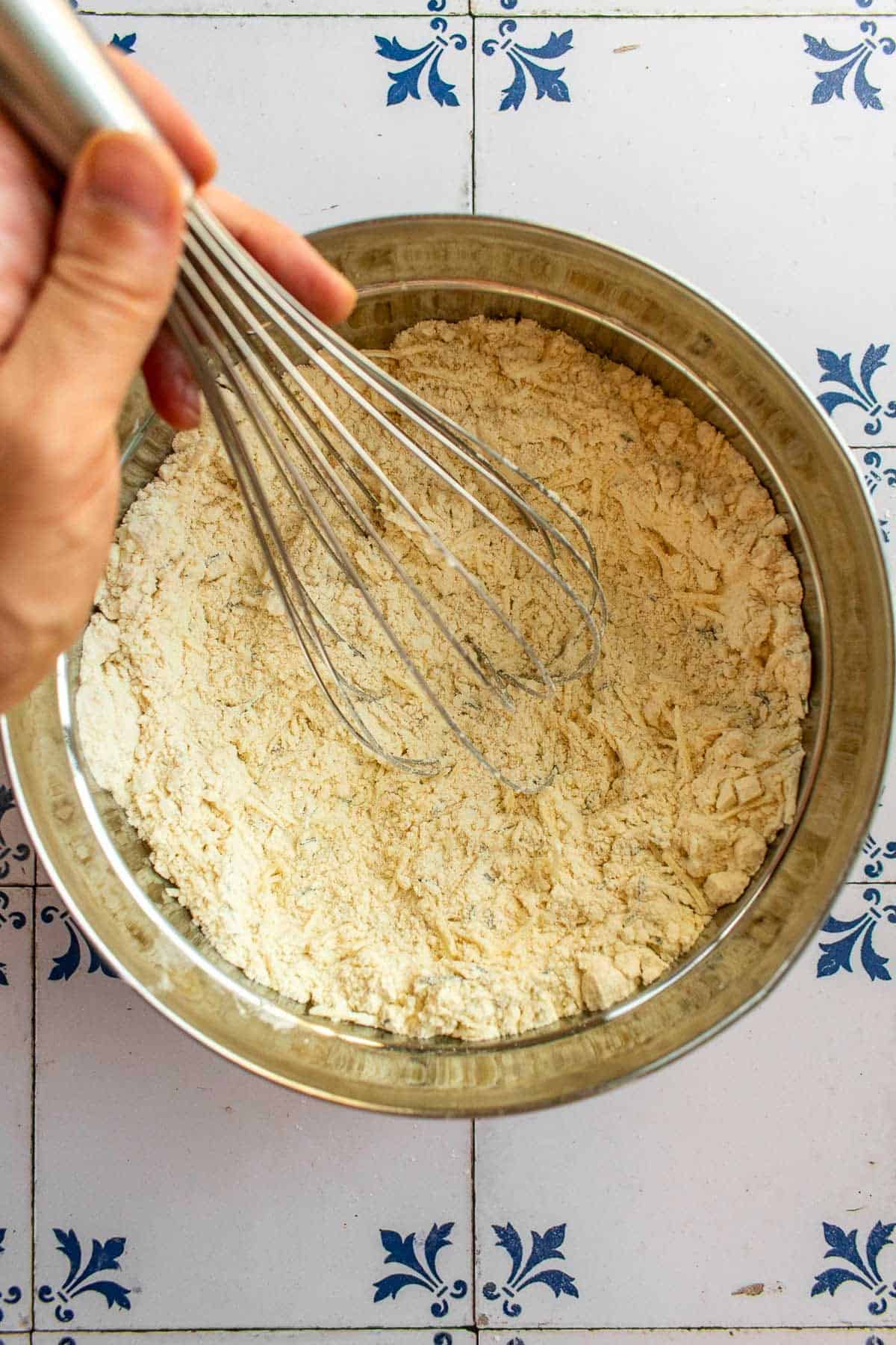A hand whisking flour, spices, and parmesan in a bowl.