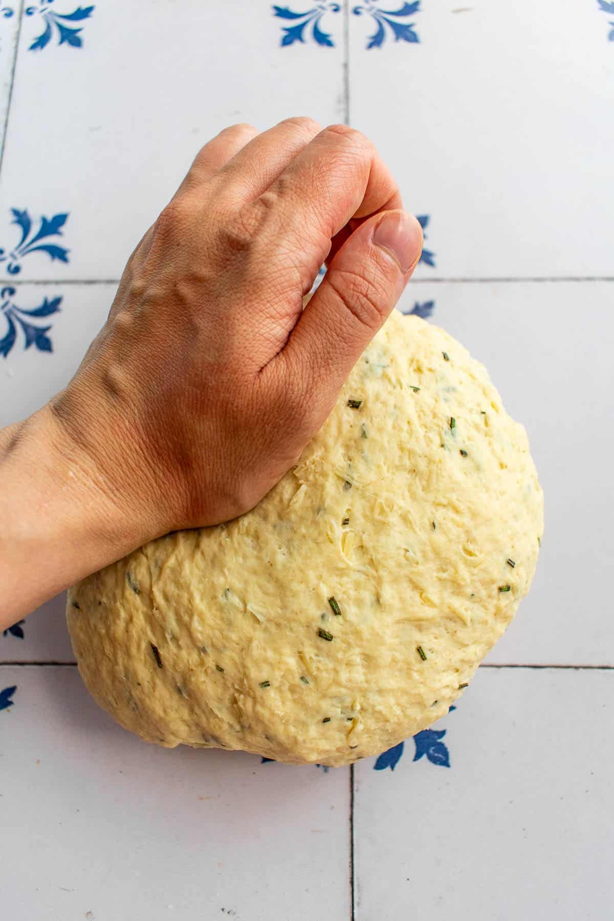 A hand kneading a ball of rosemary bread dough on a table.