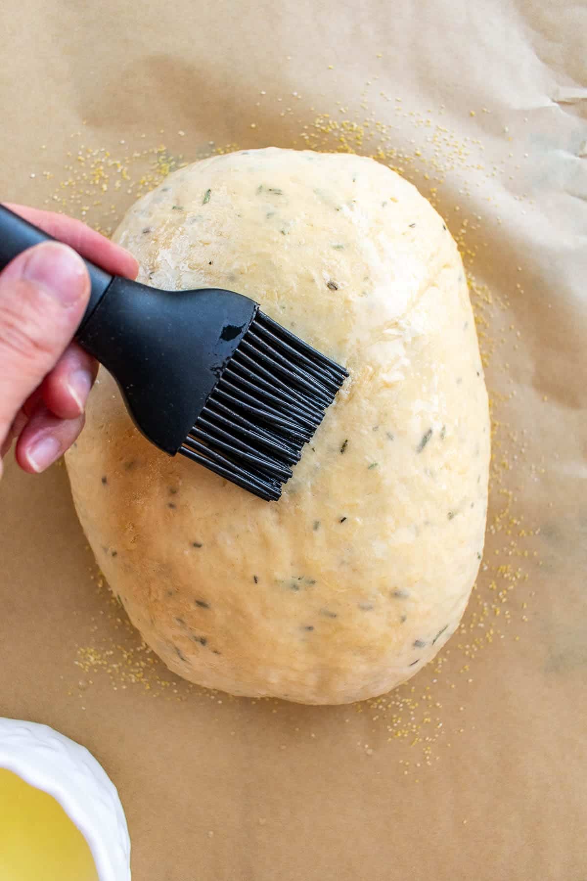 A hand brushing egg wash onto an unbaked loaf of artisan bread.