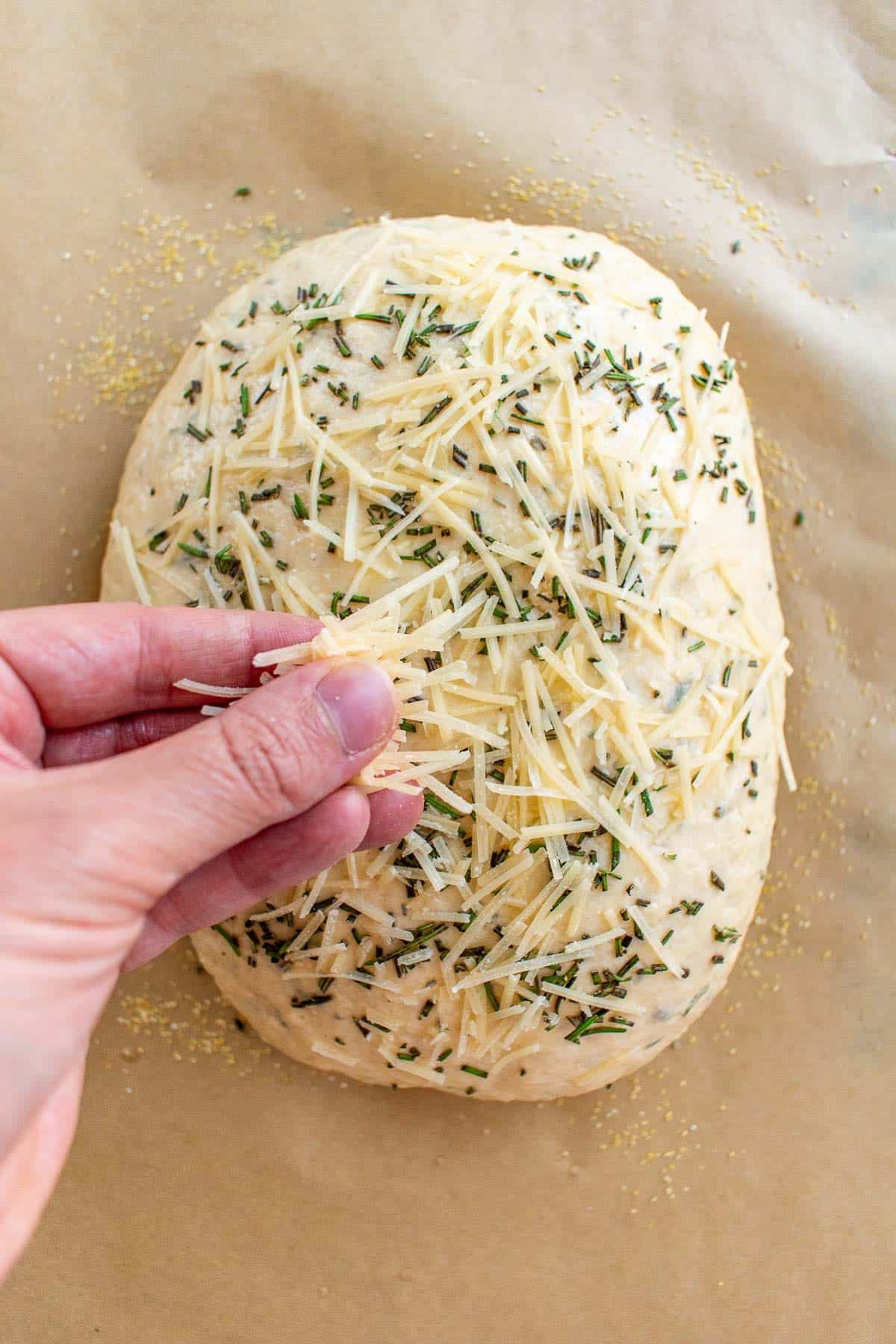 A hand sprinkling shredded Parmesan on bread dough.