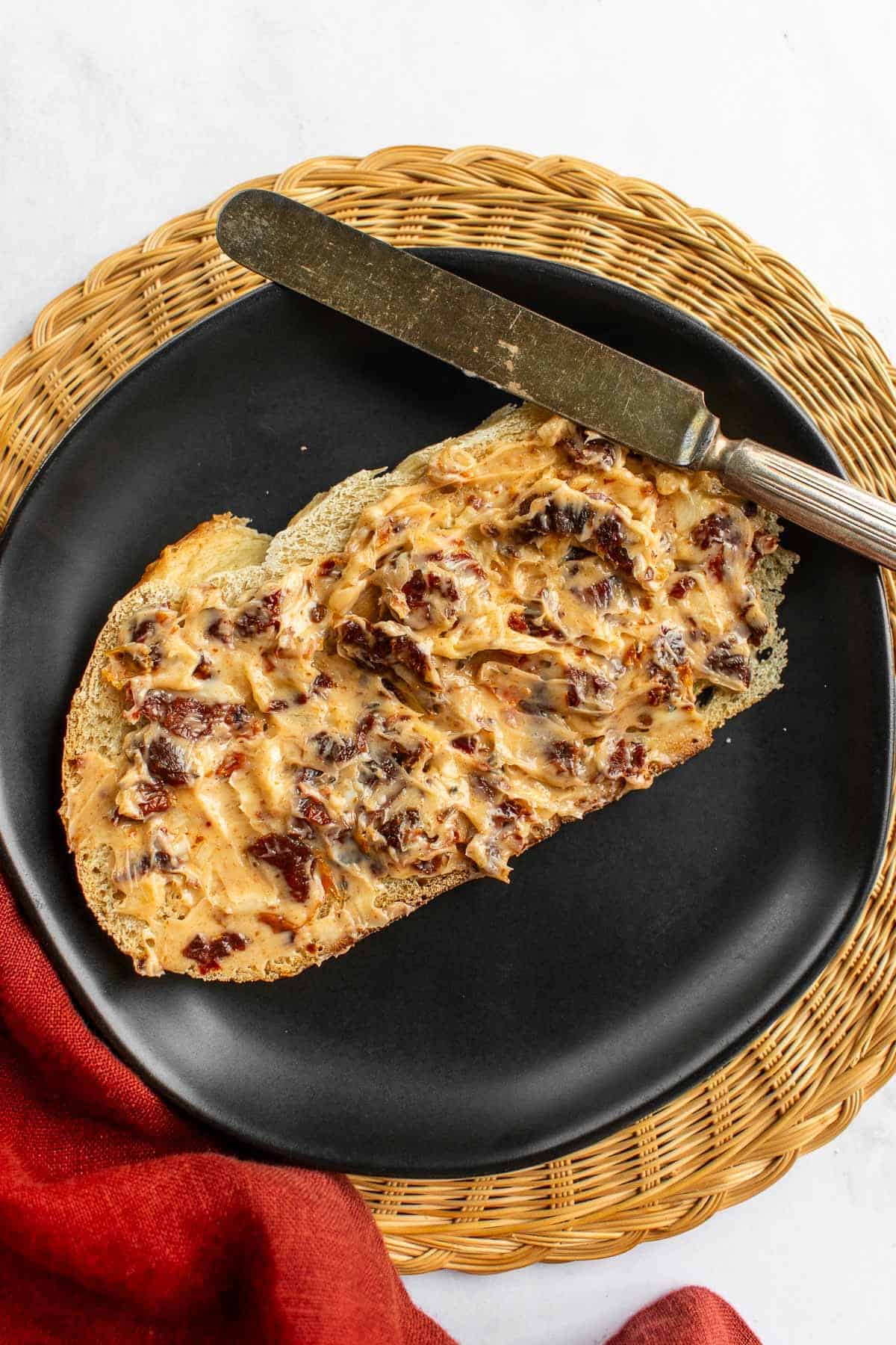 A slice of bread covered in sun dried tomato butter on a plate.