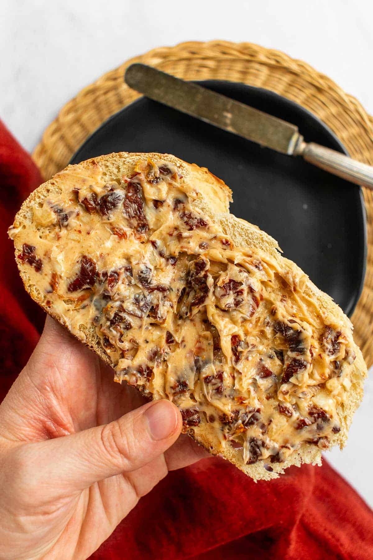 A hand holding a slice of bread covered in butter and sun dried tomatoes.