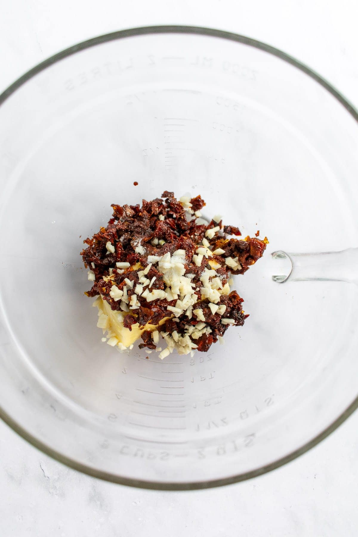 A bowl filled with butter, chopped garlic, and chopped sun dried tomatoes.