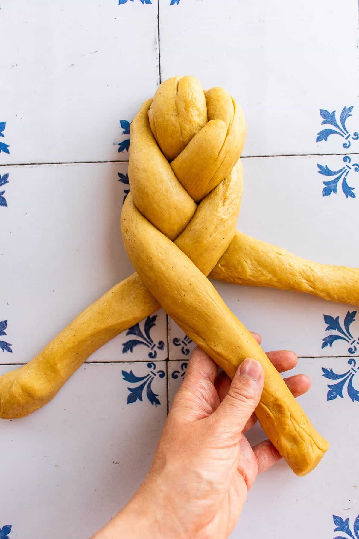 A hand braiding bread dough on a table.