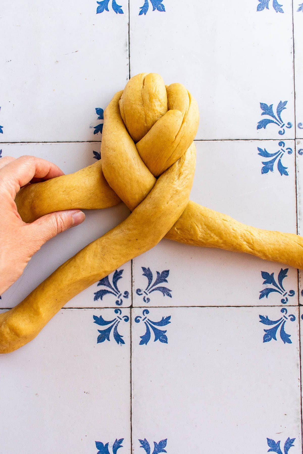 A hand braiding bread dough on a table.