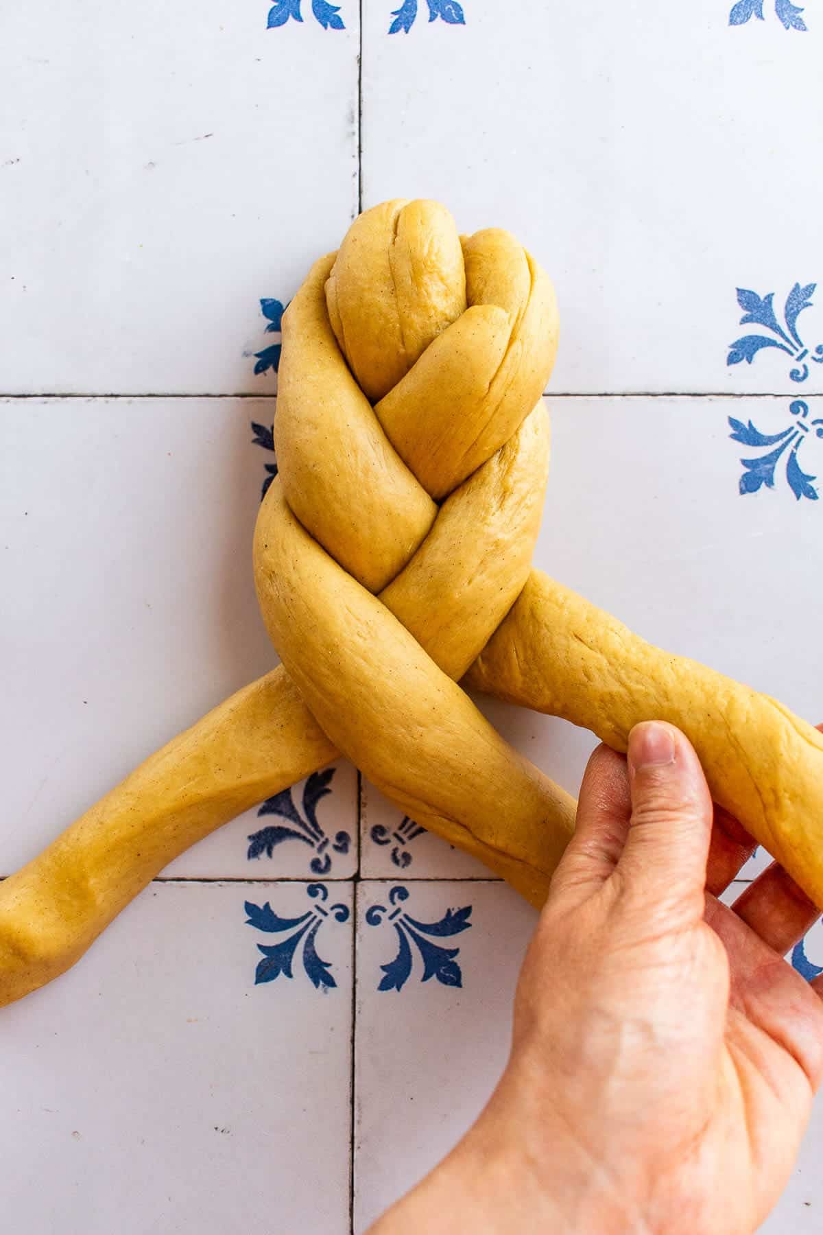 A hand braiding bread dough on a table.