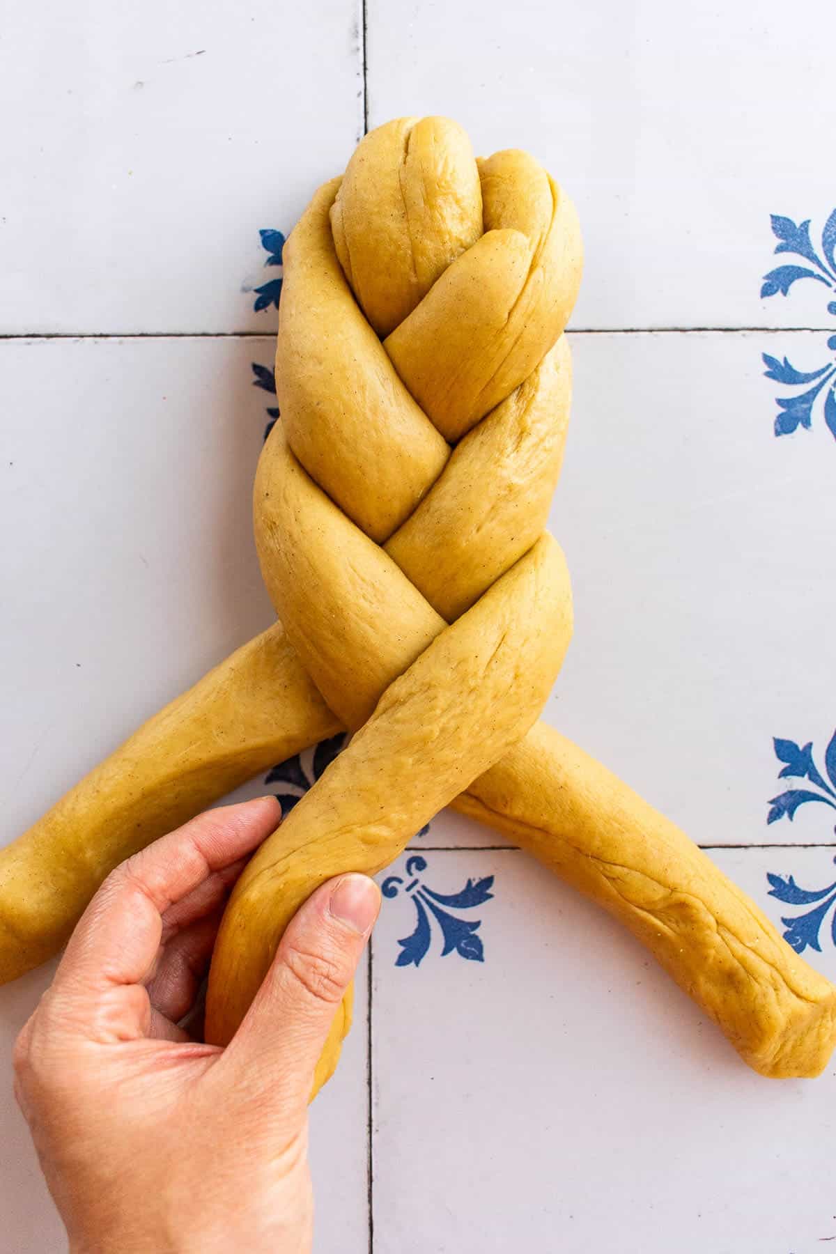 A hand braiding bread dough on a table.