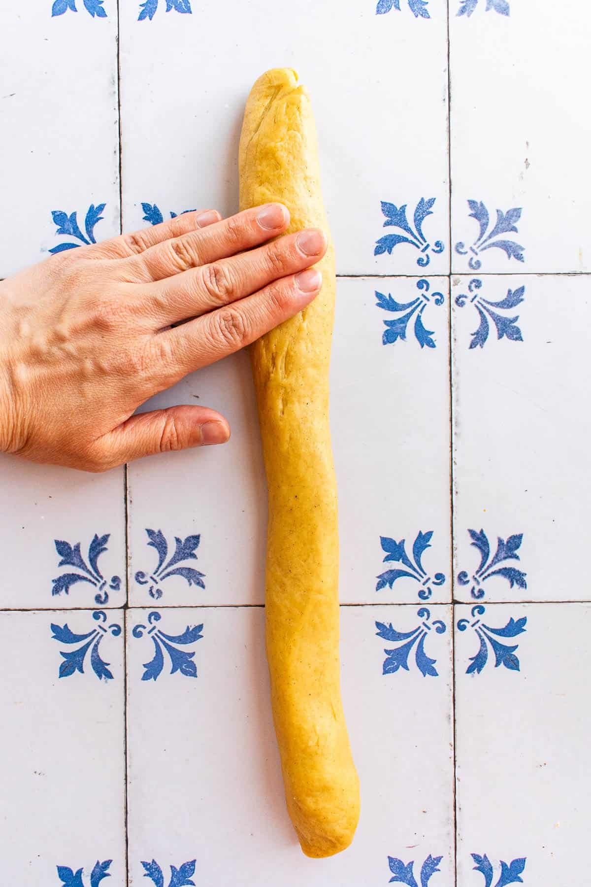 A hand rolling out a log of bread dough.
