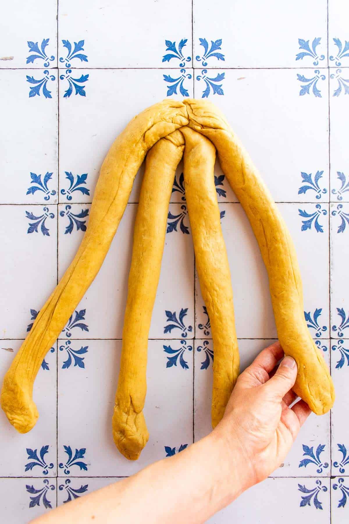 A hand braiding bread dough on a table.