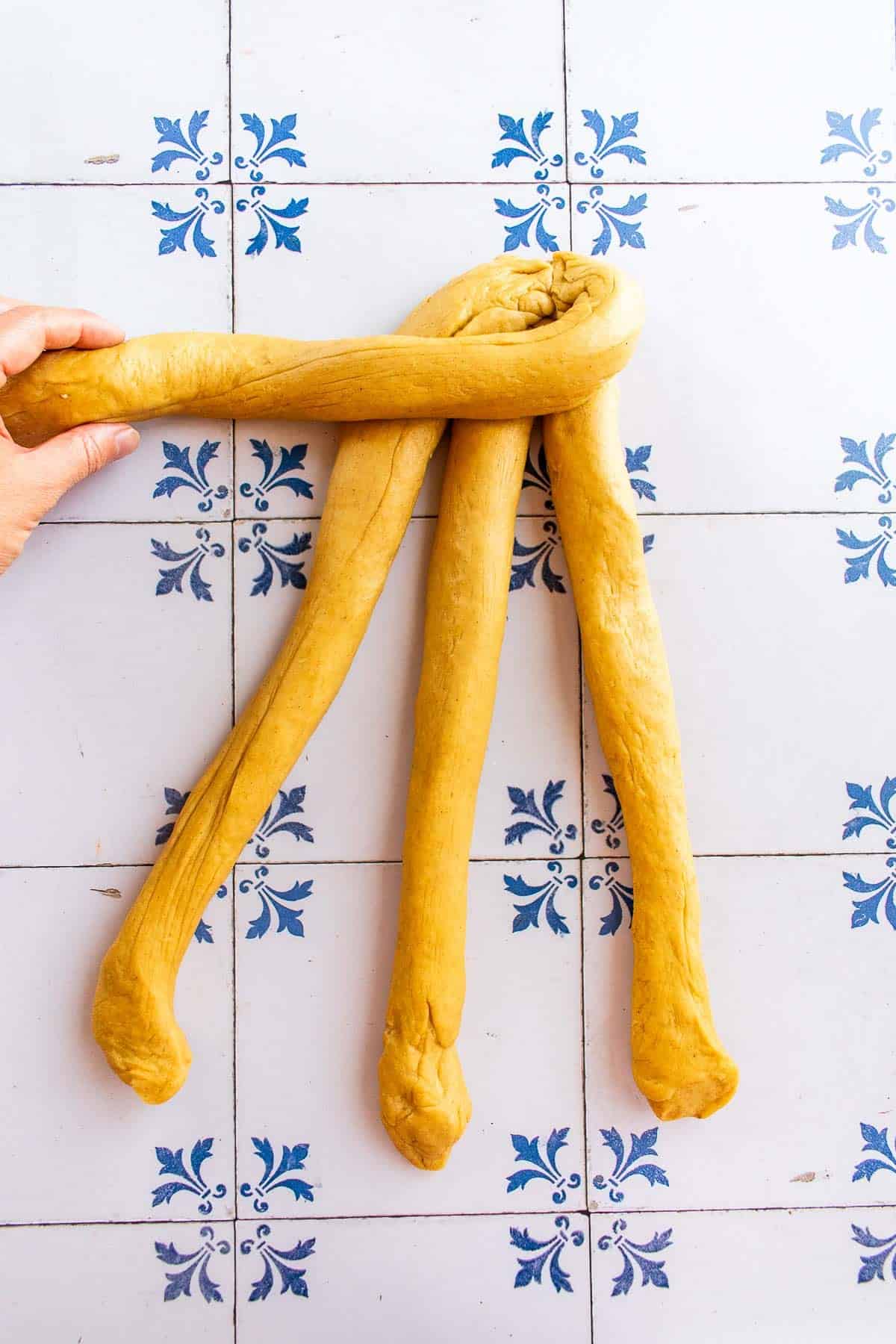 A hand braiding bread dough on a table.