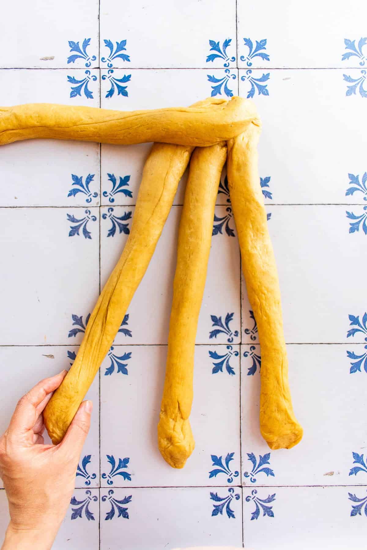 A hand braiding bread dough on a table.