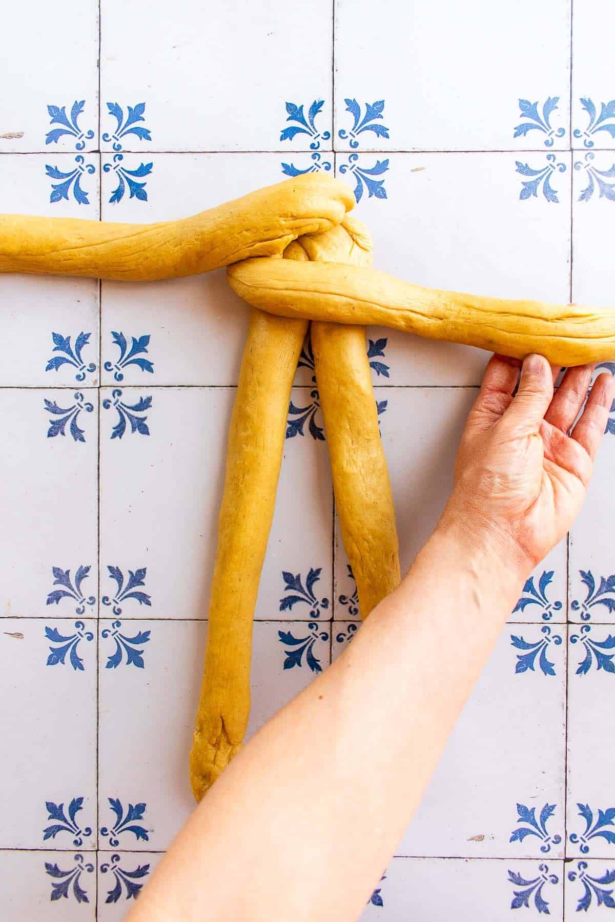 A hand braiding bread dough on a table.