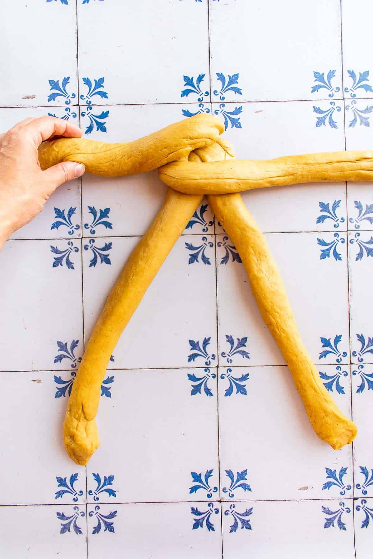 A hand braiding bread dough on a table.