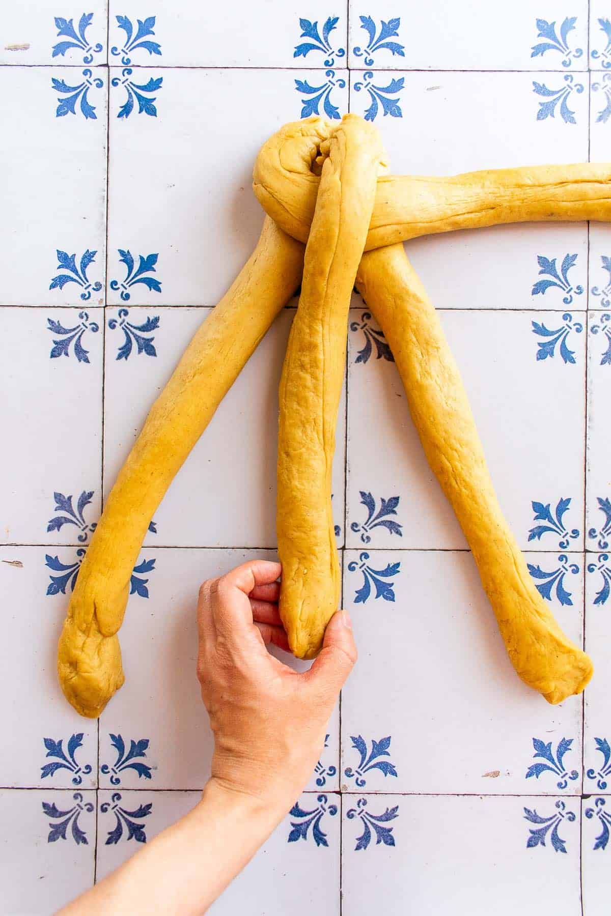 A hand braiding bread dough on a table.