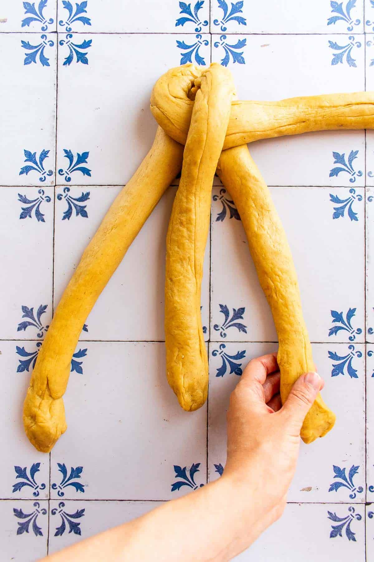 A hand braiding bread dough on a table.