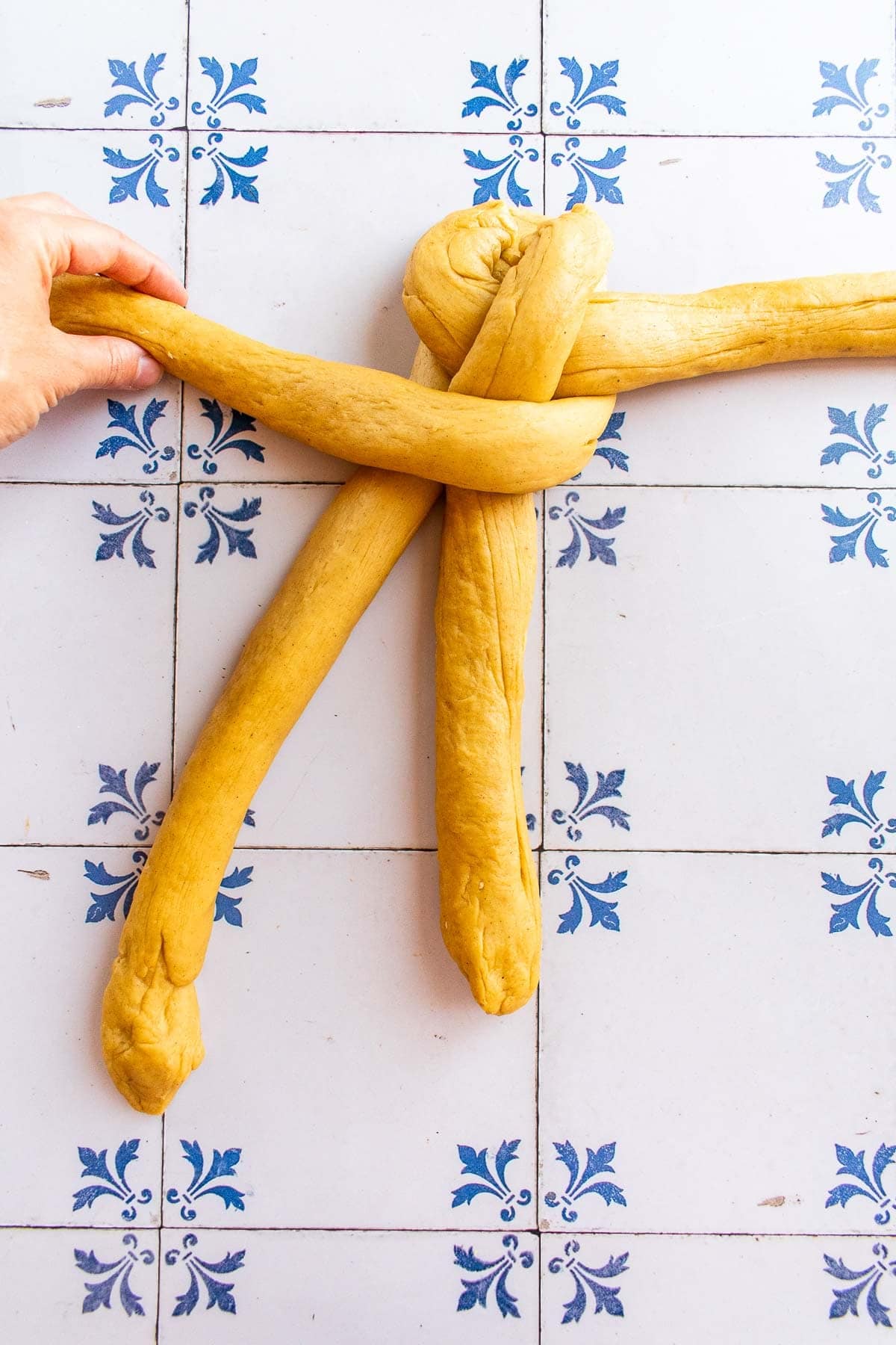 A hand braiding bread dough on a table.