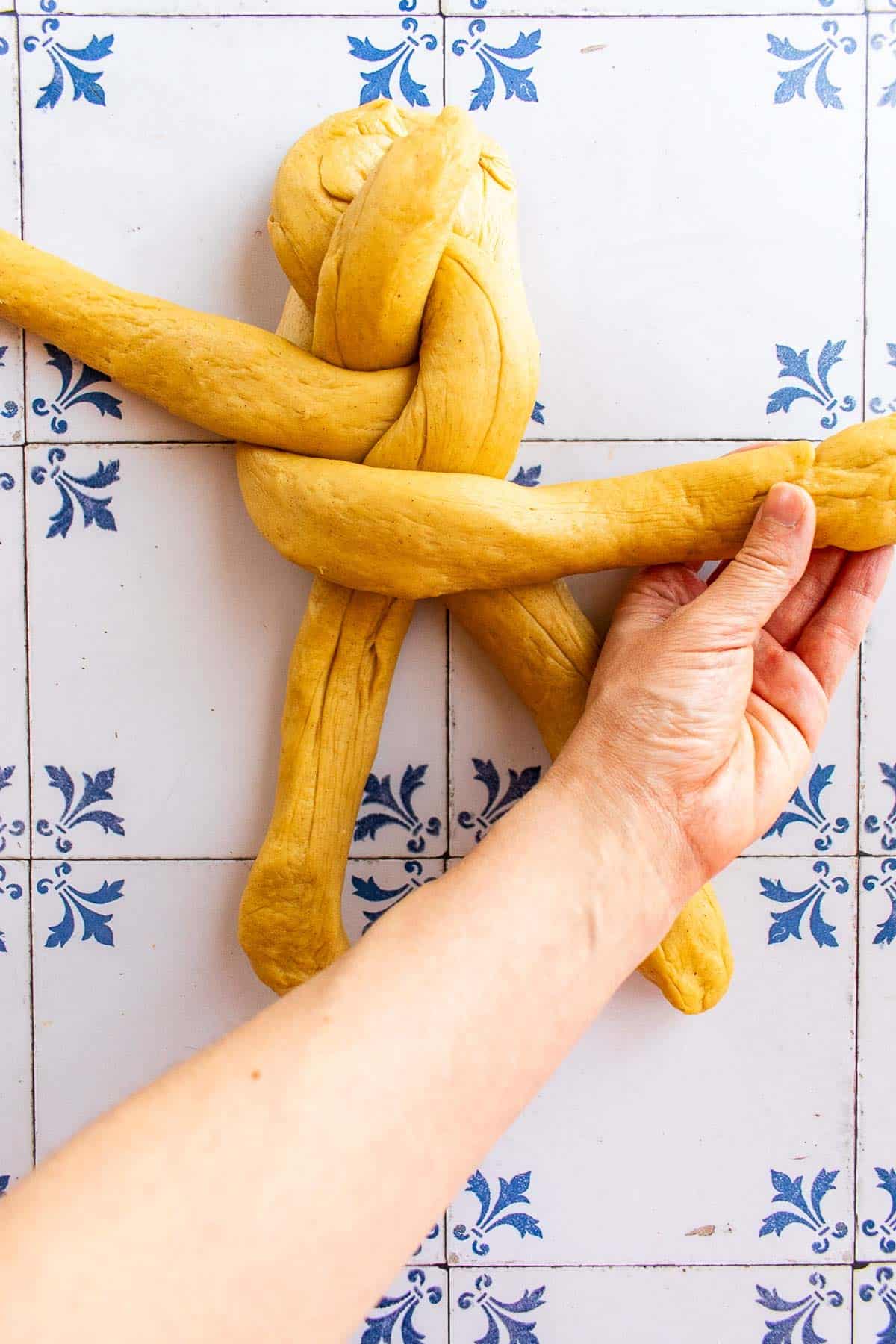 A hand braiding bread dough on a table.