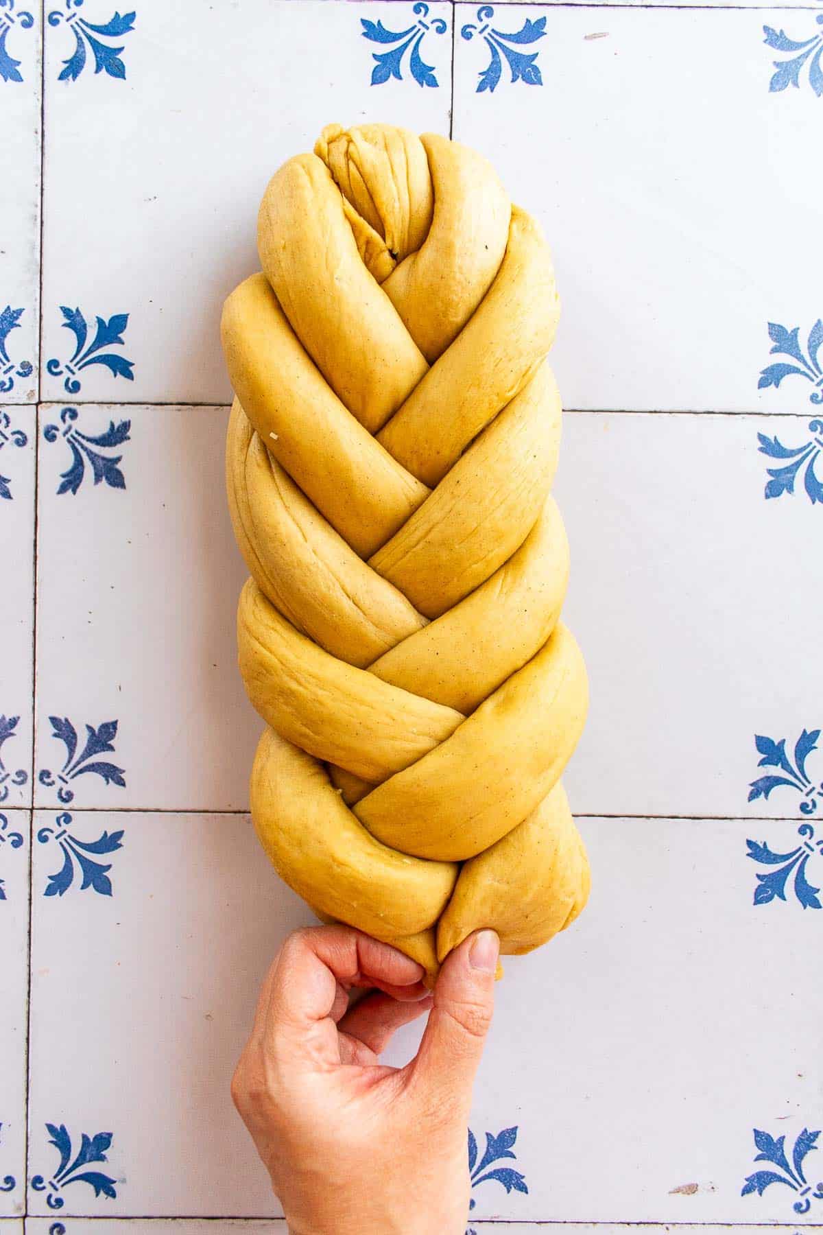 A hand braiding bread dough on a table.