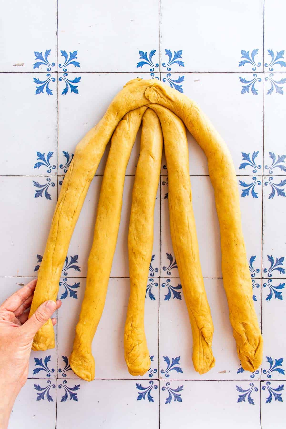 A hand braiding bread dough on a table.