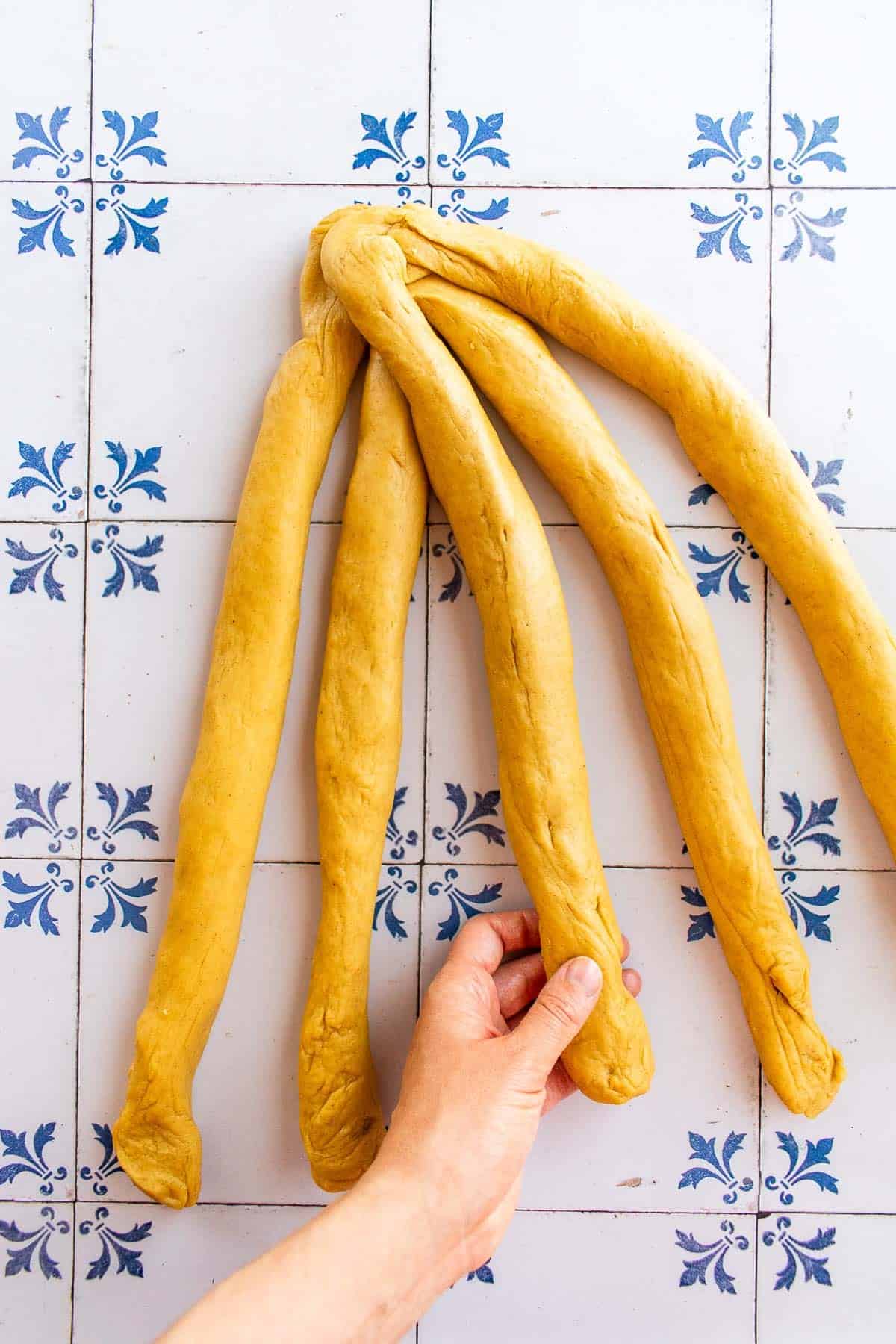 A hand braiding bread dough on a table.
