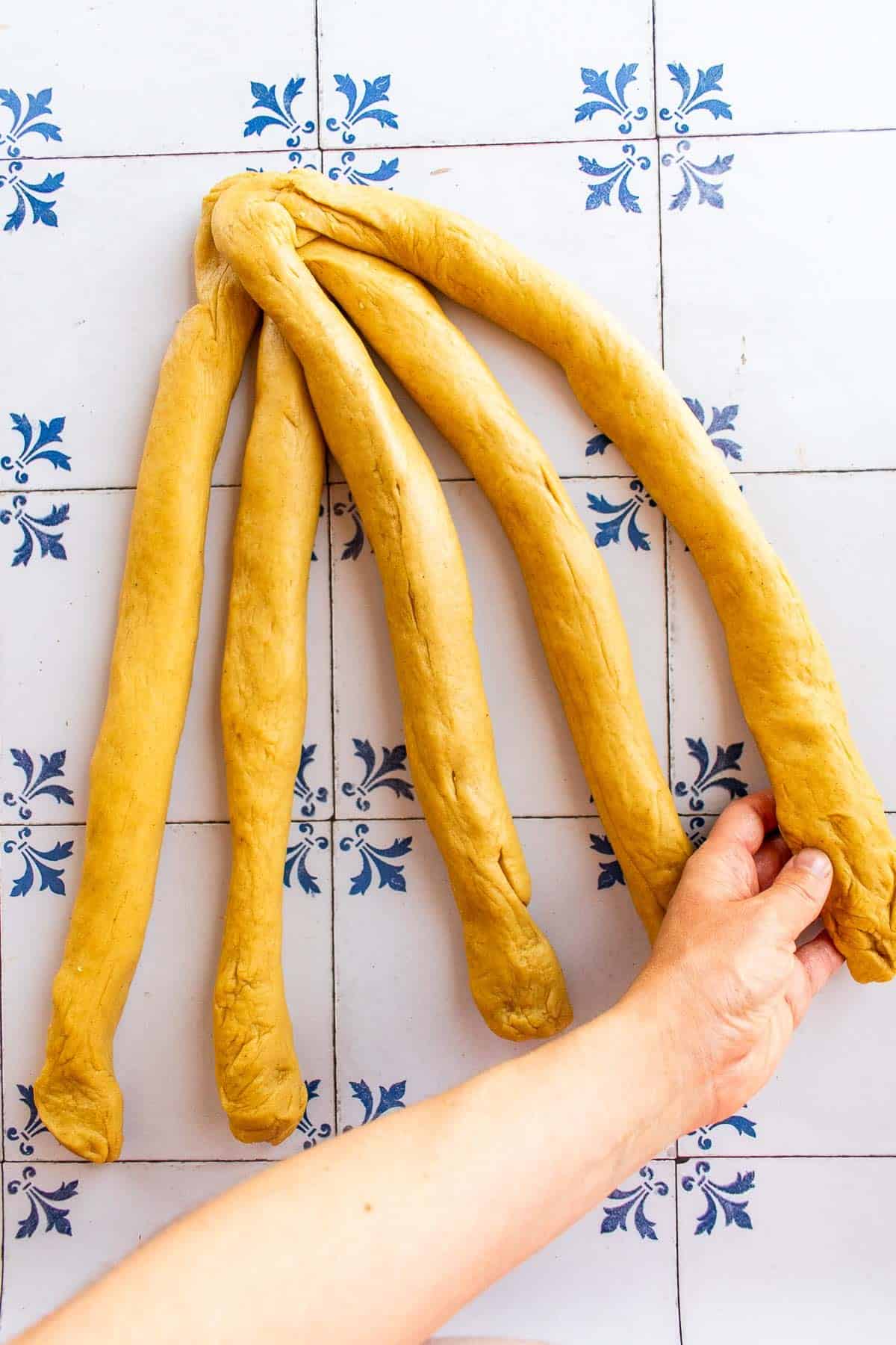 A hand braiding bread dough on a table.