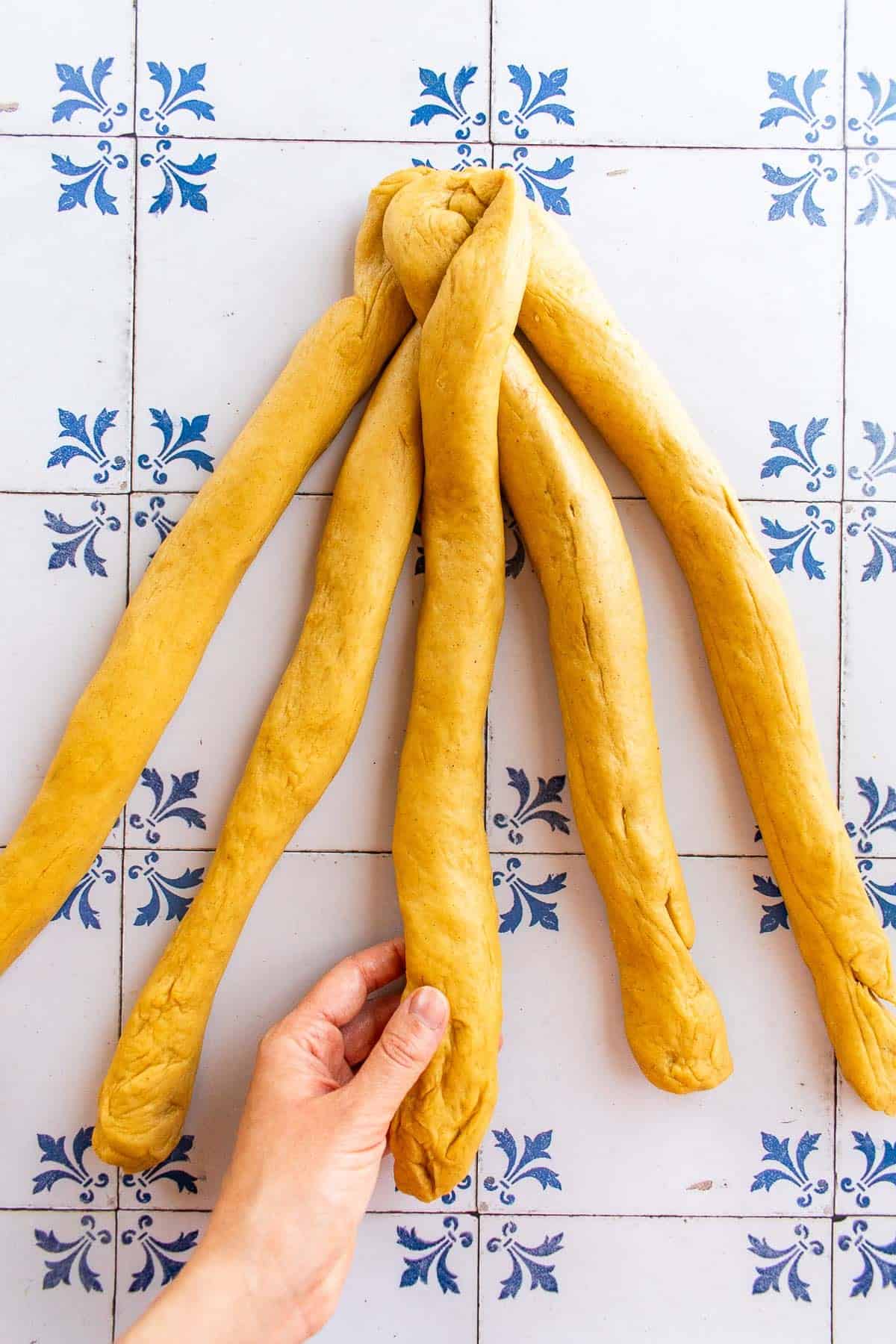 A hand braiding bread dough on a table.