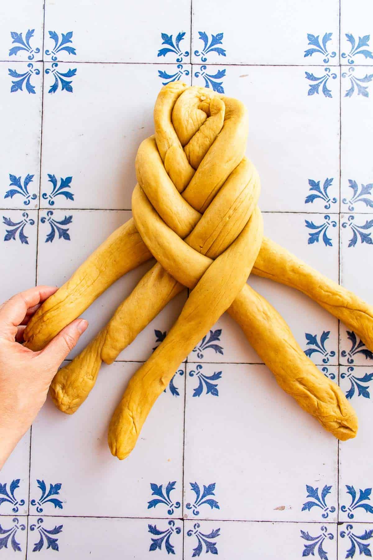 A hand braiding bread dough on a table.