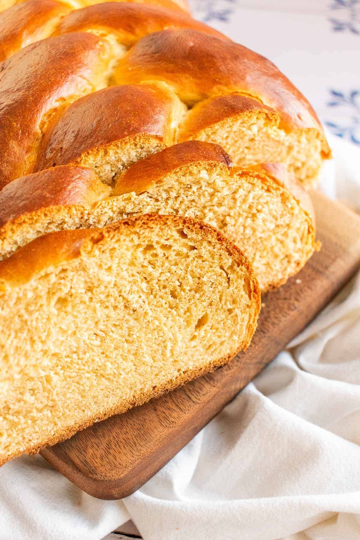 A sliced loaf of braided bread on a wood board.