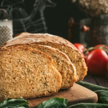 Two slices of bread filled with dried basil and sundried tomatoes on a wooden board.