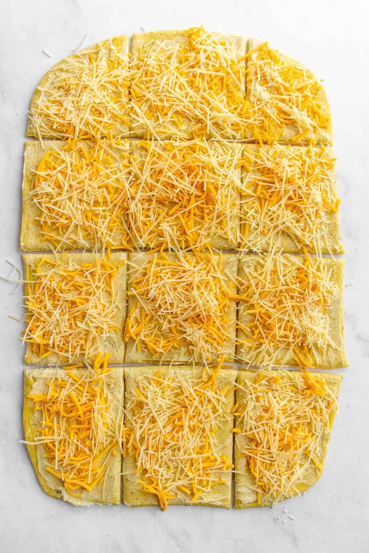 Twelve squares of bread dough topped with shredded cheese.