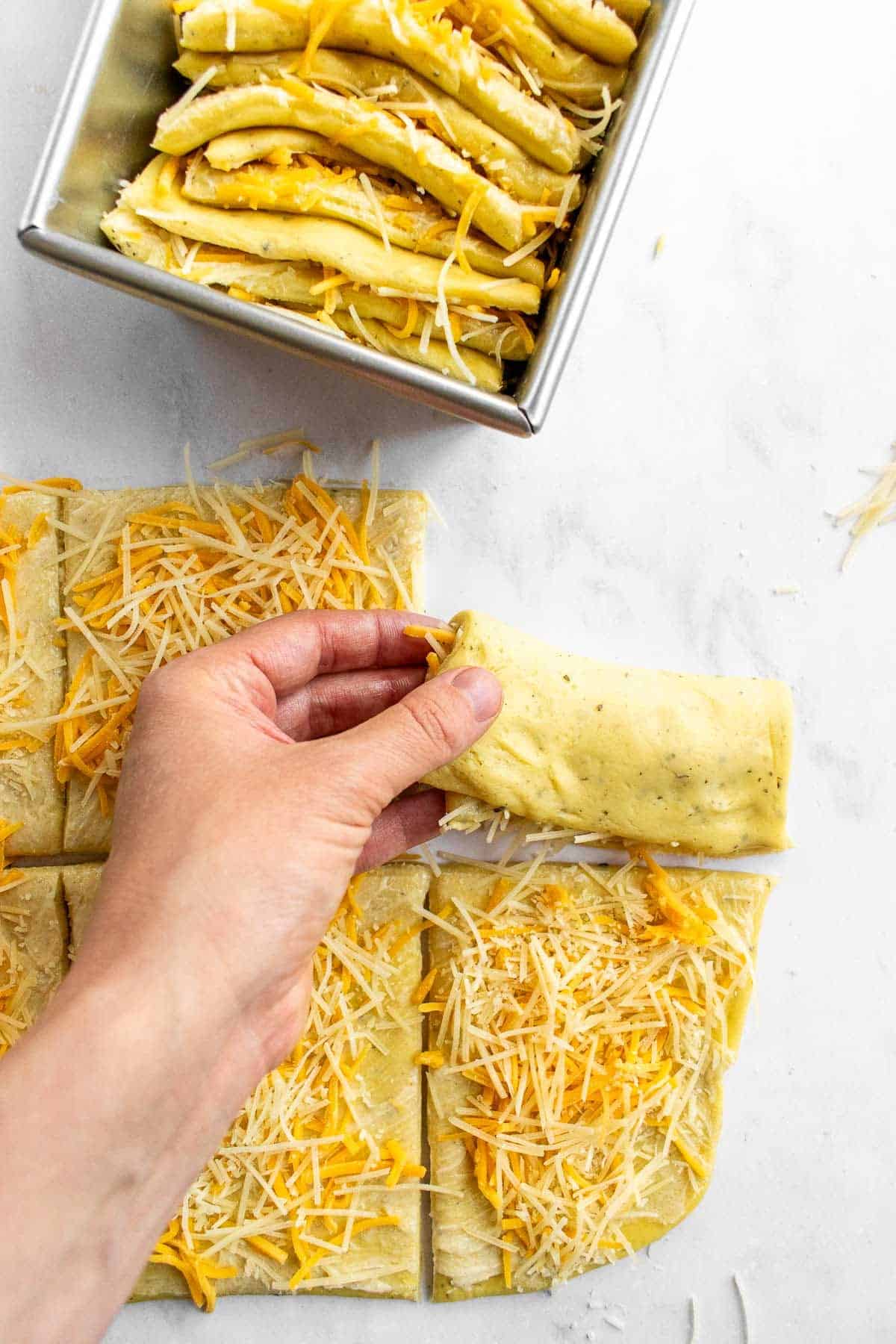 A hand folding squares of cheese-filled dough in half.