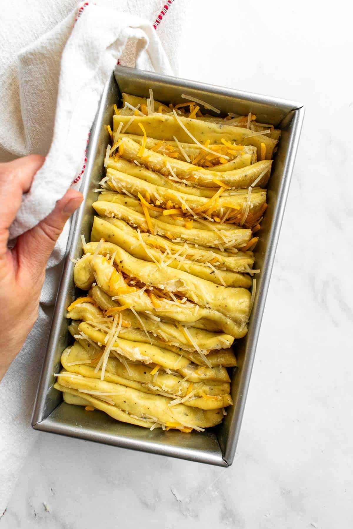 An unbaked loaf of cheesy pull apart bread in a metal tin.