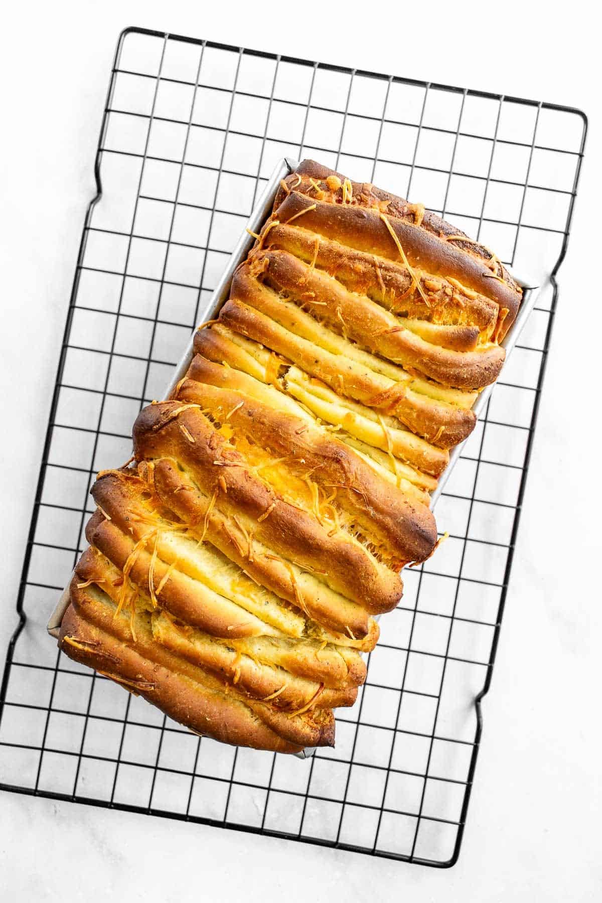 A baked loaf of cheesy pull apart bread on a cooling rack.