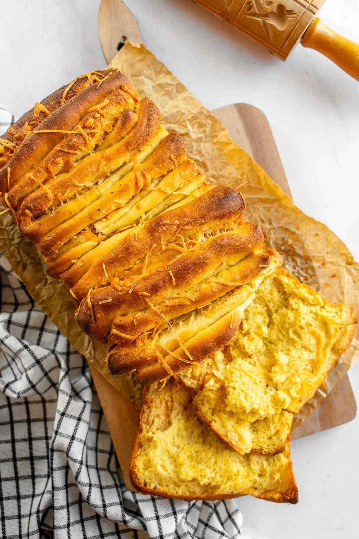 A loaf of cheese pull apart bread on a wood cutting board on a linen.