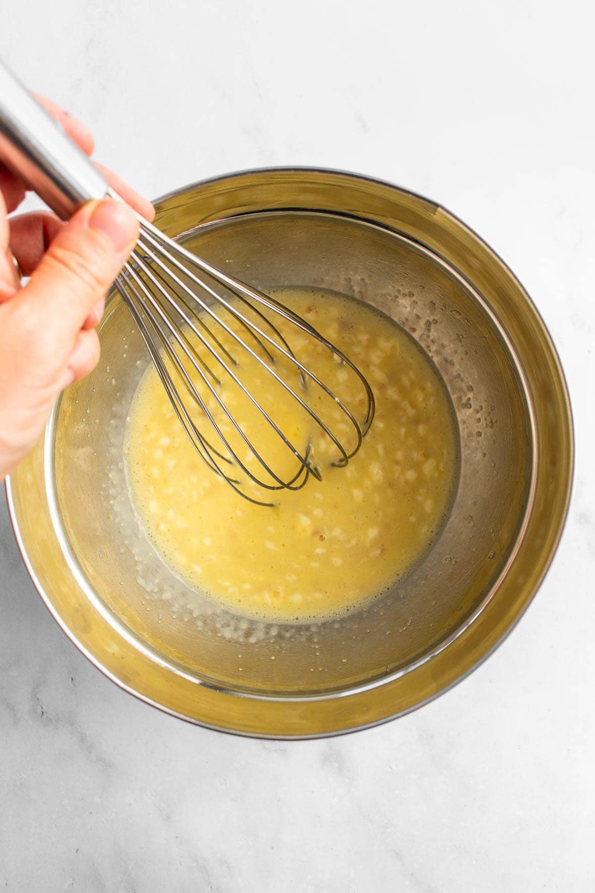 A hand whisking milk, butter, eggs, yeast, and sugar in a bowl.