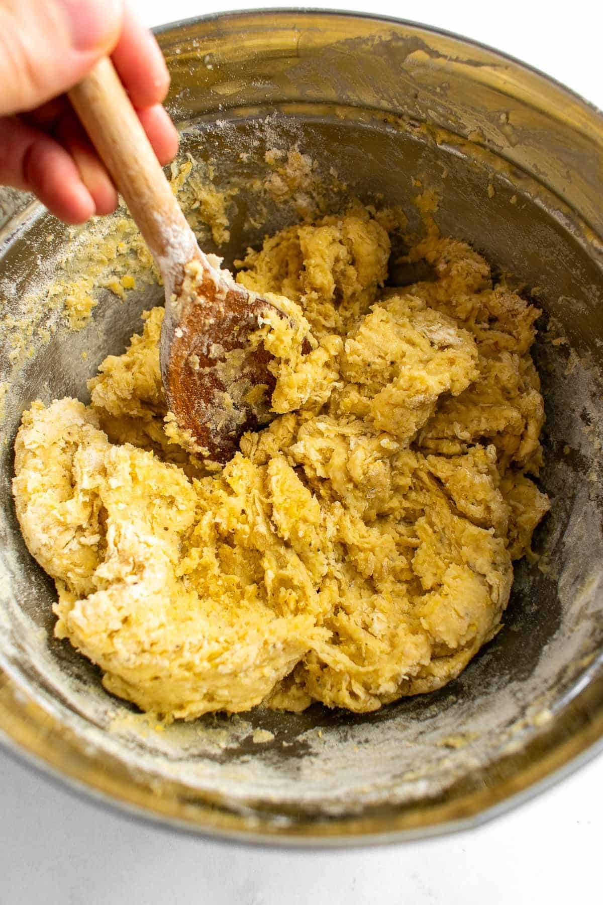 A hand mixing bread dough in a bowl with a wooden spoon.