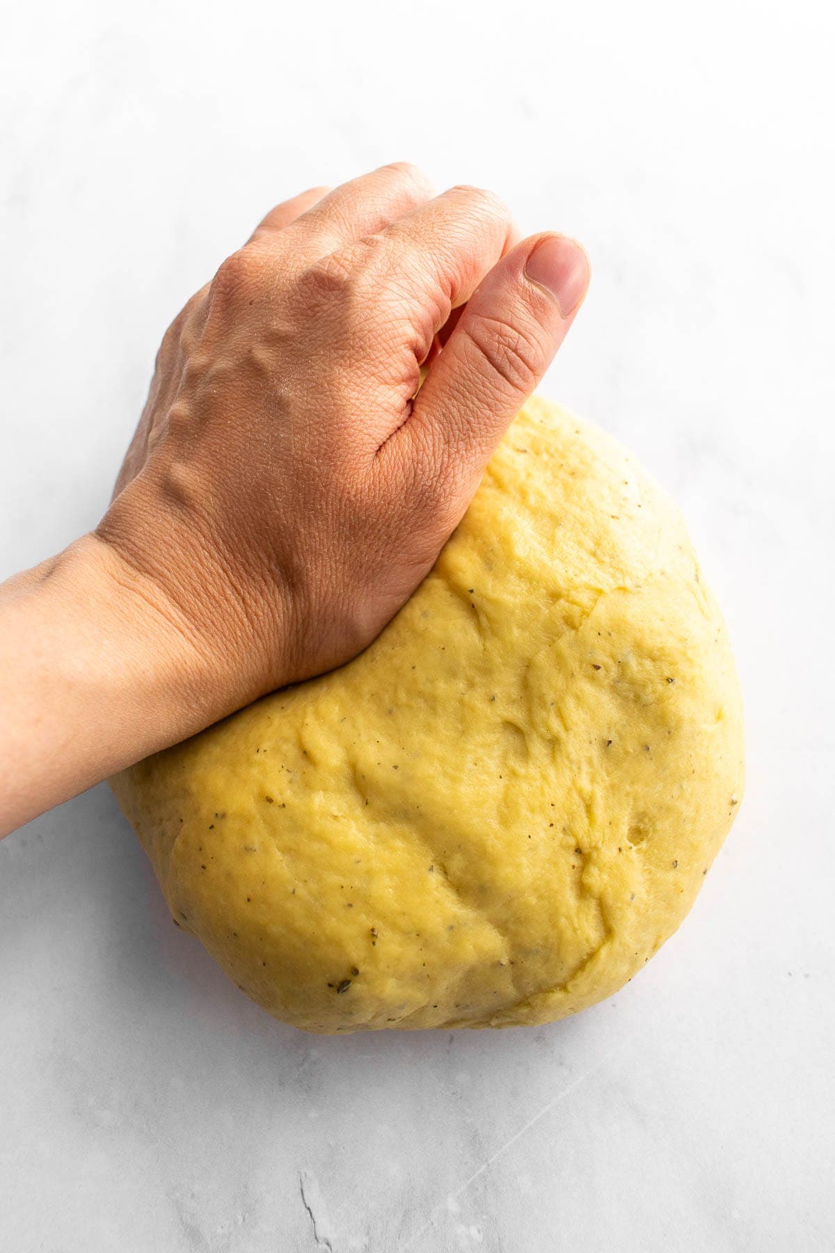 A hand kneading a ball of bread dough on a marble surface.