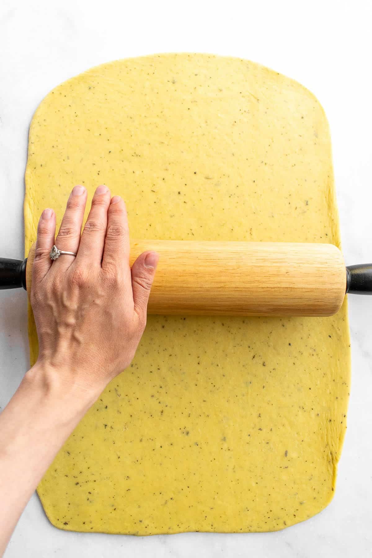 A hand rolling out bread dough with a rolling pin.