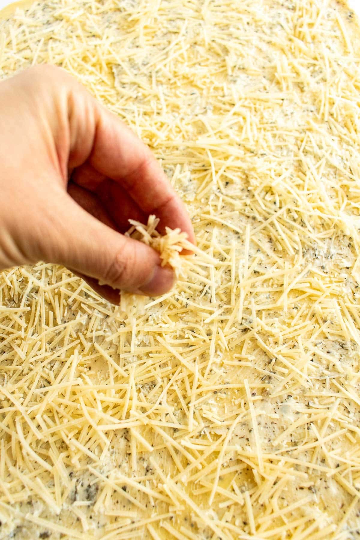 A hand sprinkling shredded cheese onto bread dough.