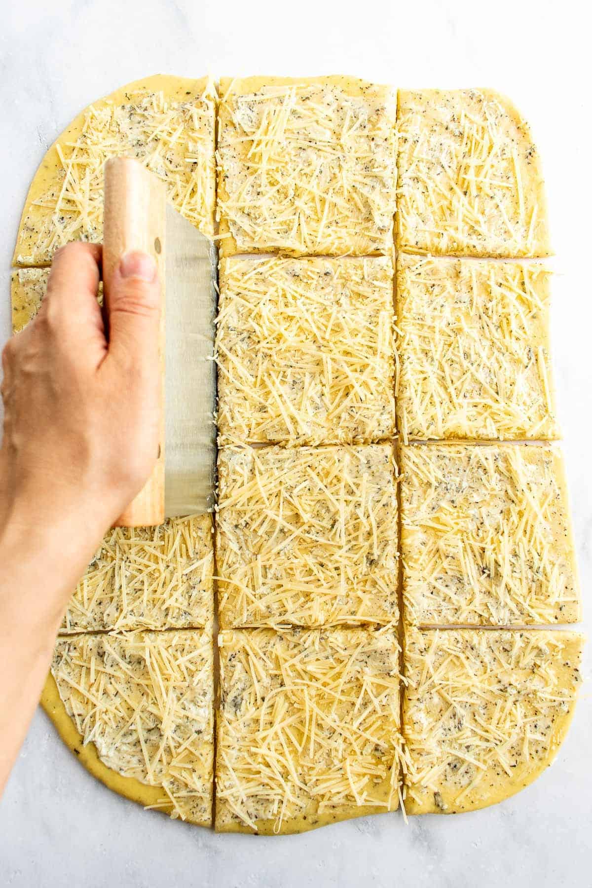 A hand cutting 12 squares into rolled-out garlic bread dough.
