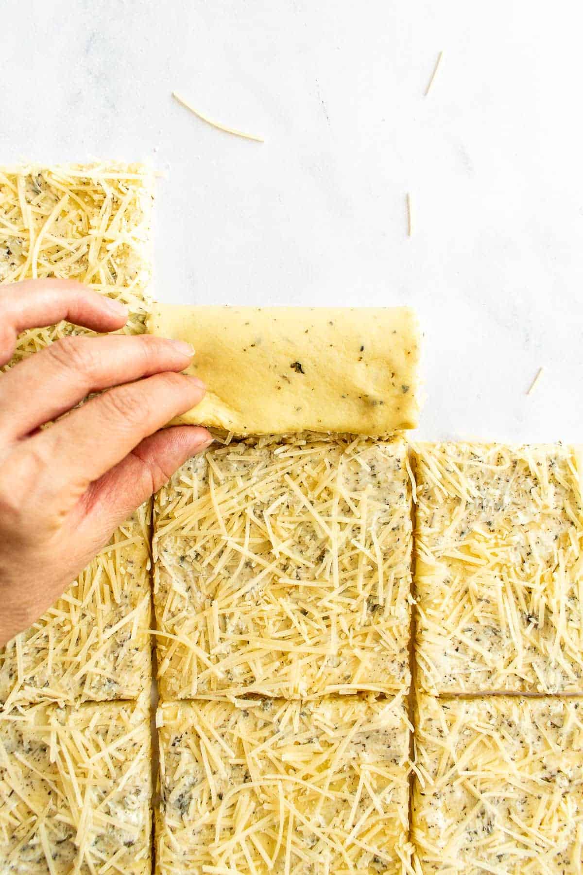 Flat squares of cheese-covered garlic bread dough being folded in half.