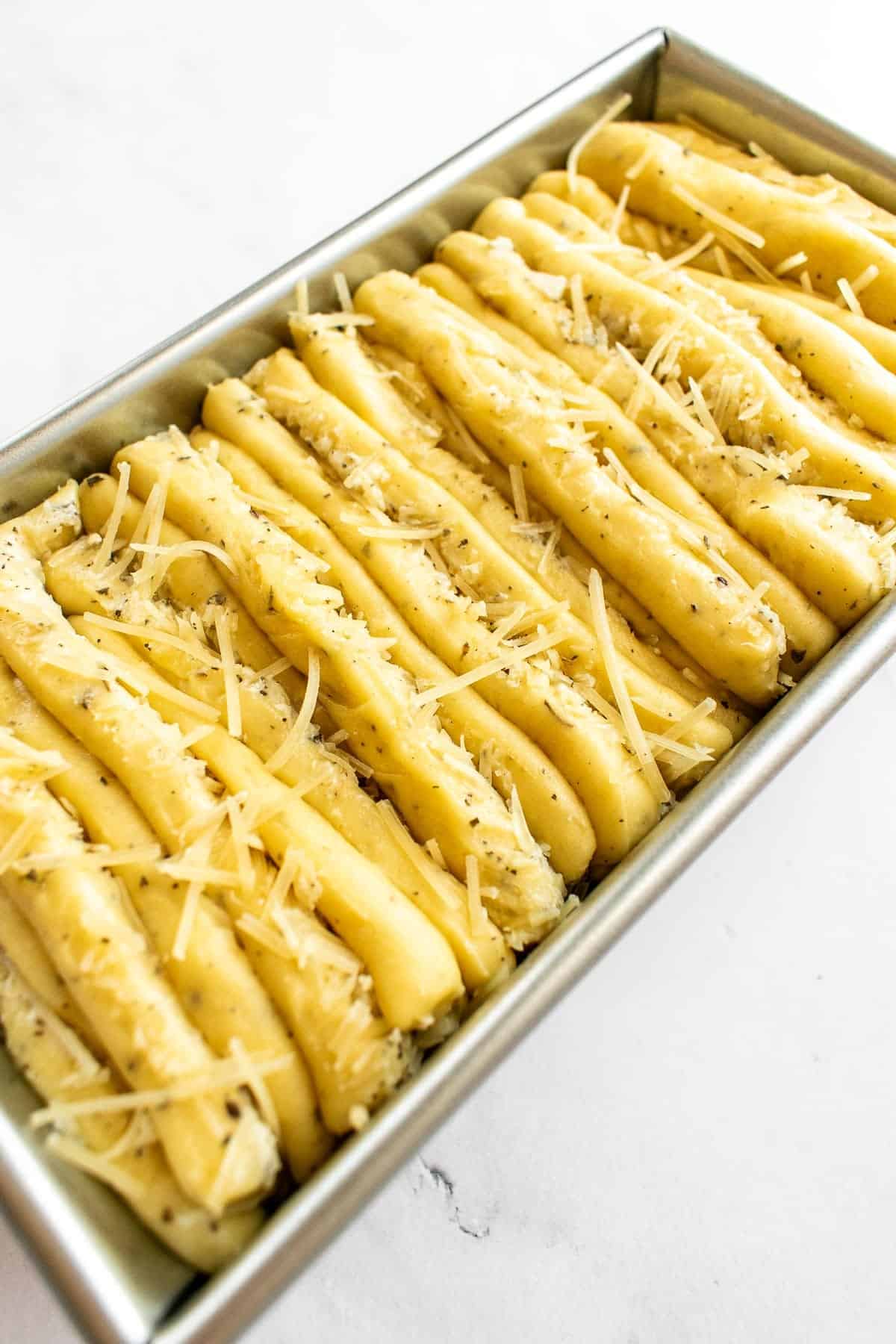 Unbaked garlic pull apart bread dough in a metal loaf pan.