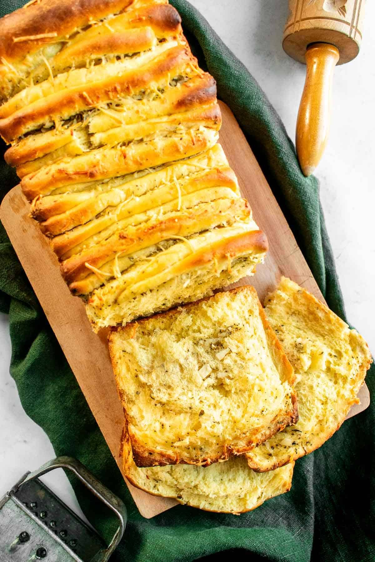 Slices of garlic bread next to the rest of the loaf on a wood board on a linen.