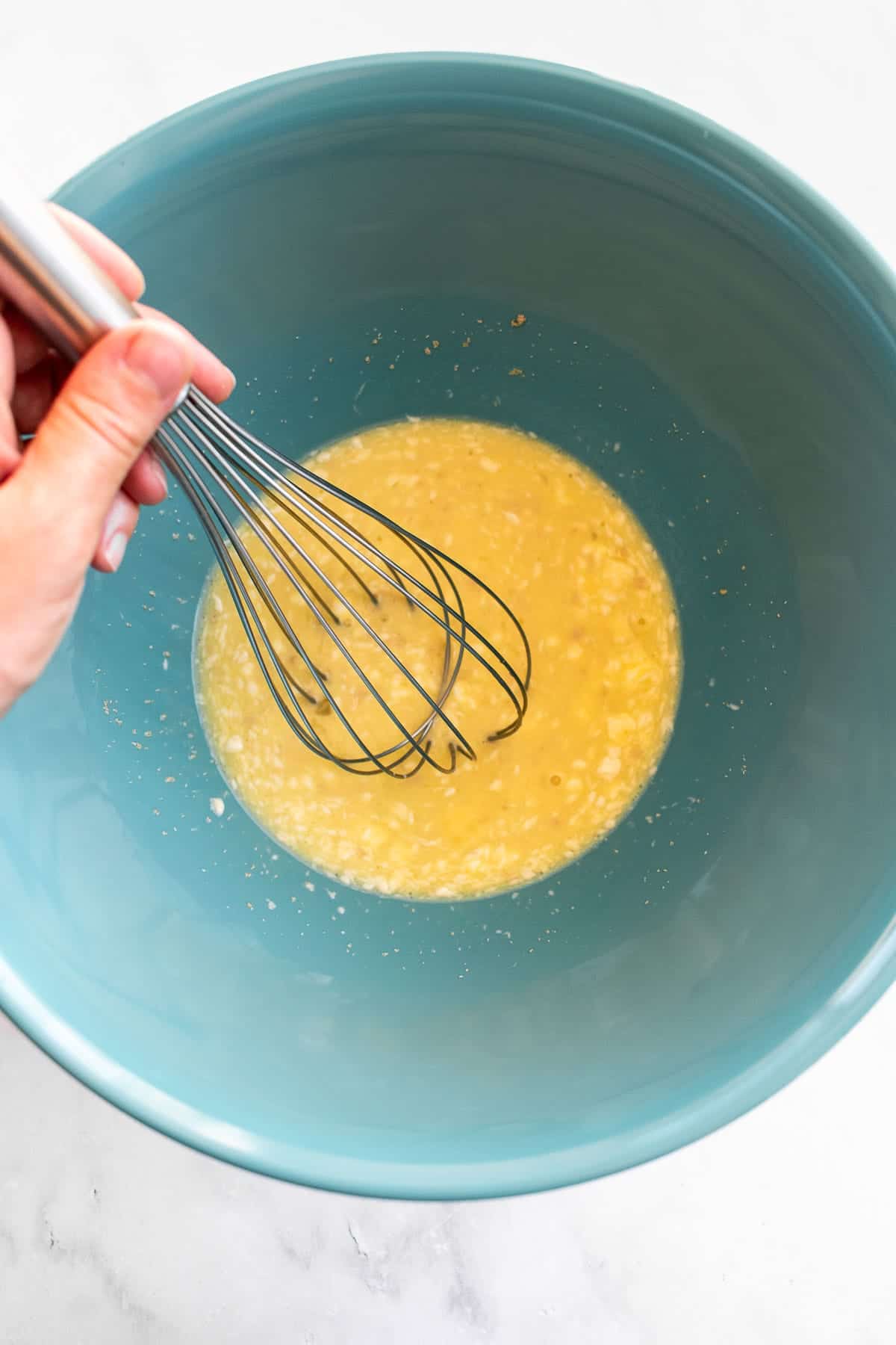 A hand whisking butter, eggs, and milk in a blue bowl.