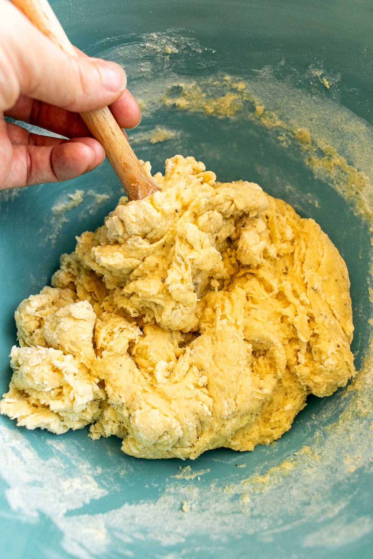 A hand mixing bread dough in a bowl with a wooden spoon.