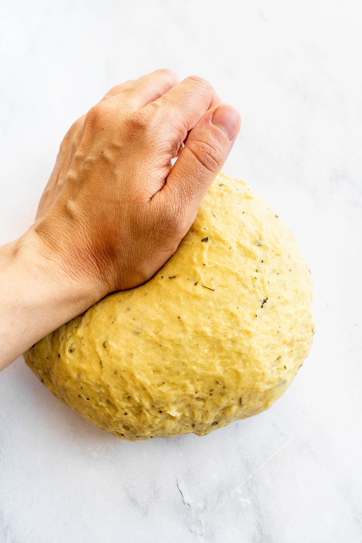 A hand kneading a ball of elastic bread dough on a counter.