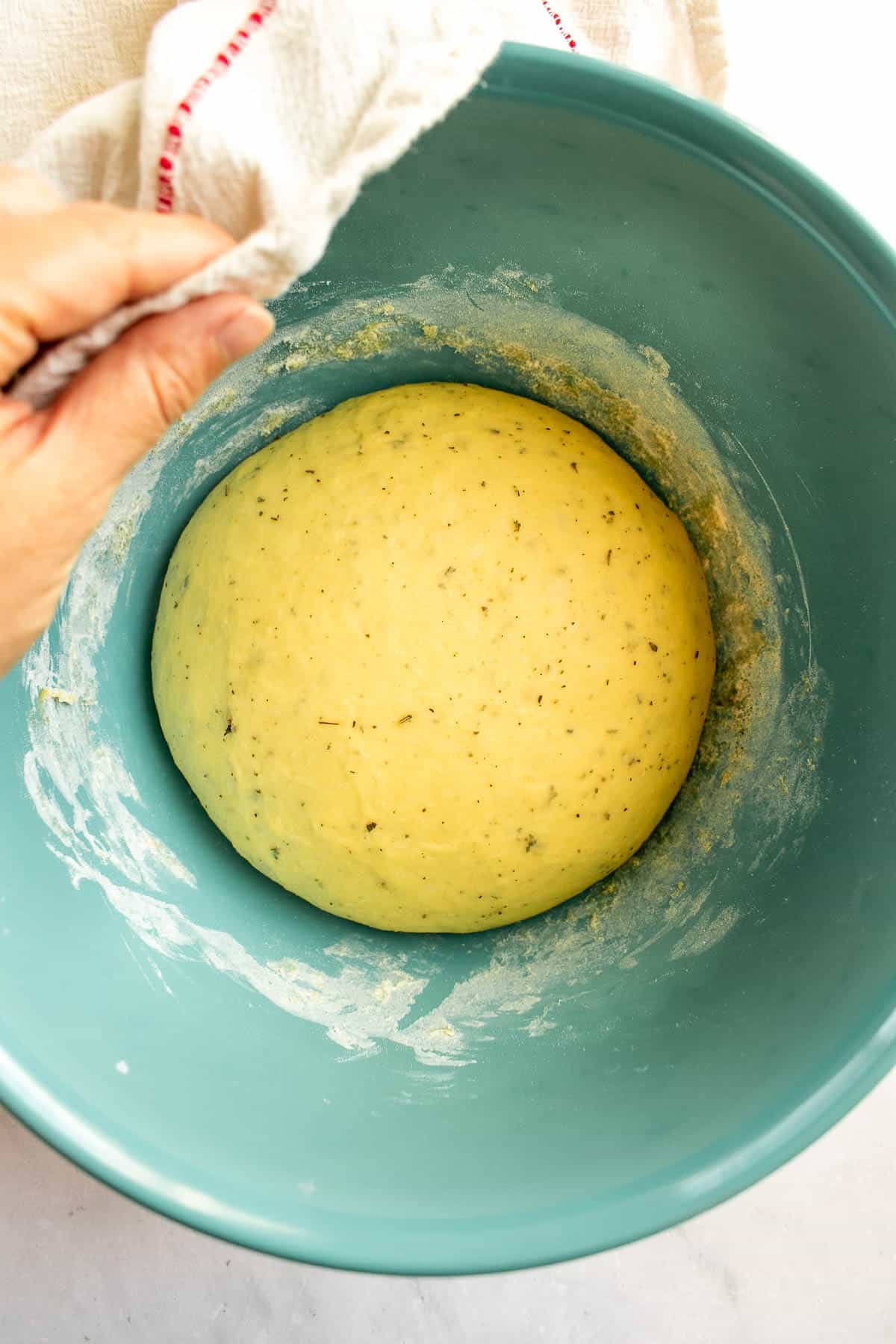 A ball of risen herb bread dough in a bowl.