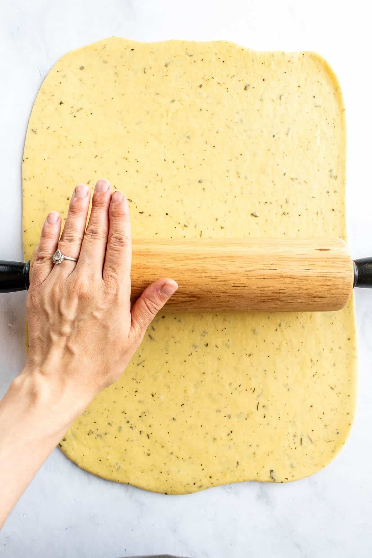 A hand rolling out bread dough with a wooden rolling pin.